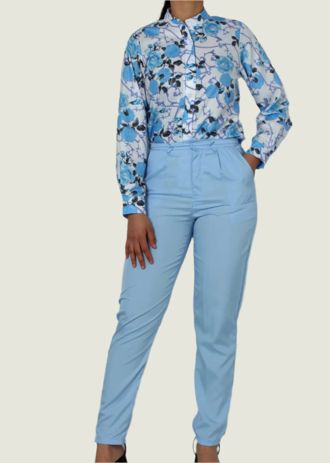 Person wearing a floral blouse and light blue pants against a plain background